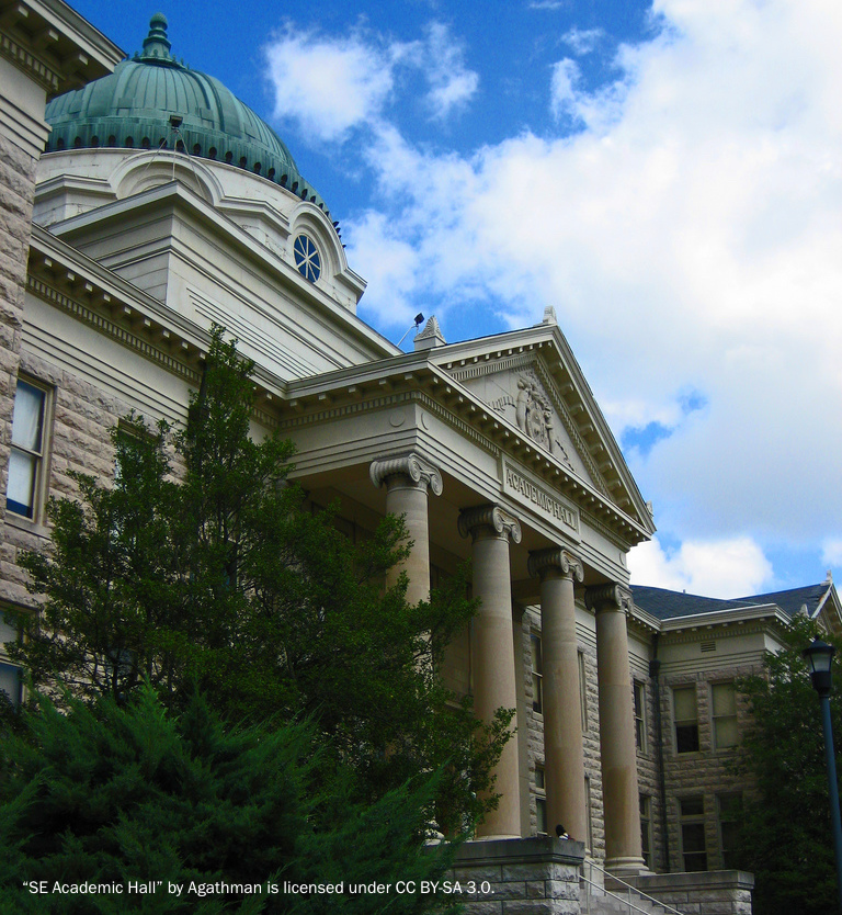 Photograph of a historic university building of white stone built in classical style with four marble columns at the main entrance and a copper dome.