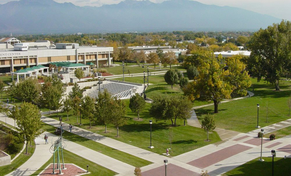 Campus grounds with trees, sidewalks, and an amphitheater, with several large buildings in the background.